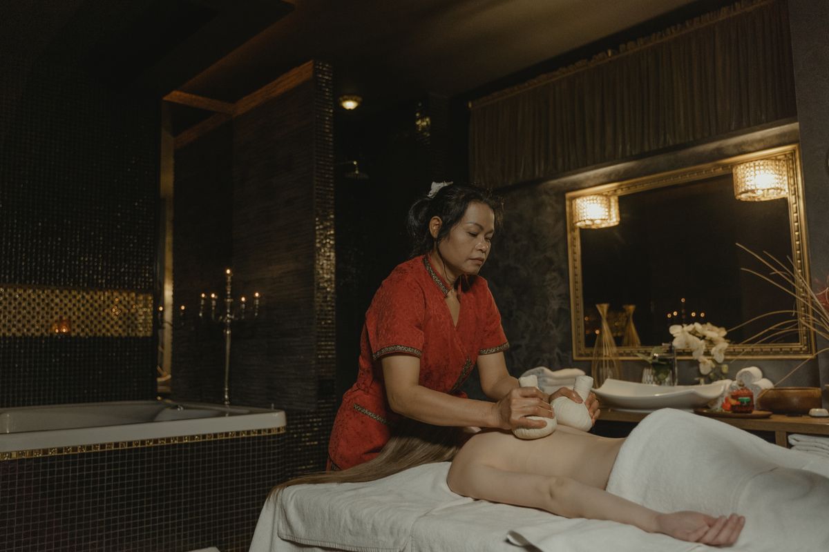 Terapist loş bir SPA odasında danışanına bitki keseleriyle masaj yaparken